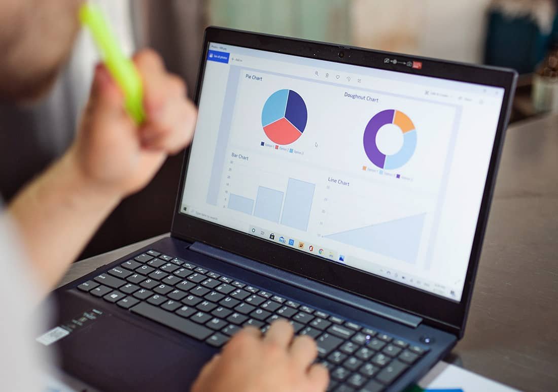 A person holding a highlighter is analyzing data on a laptop screen. The screen displays various charts, including pie charts, a doughnut chart, a bar chart, and a line chart. The focus is on the visual data representations on the laptop.